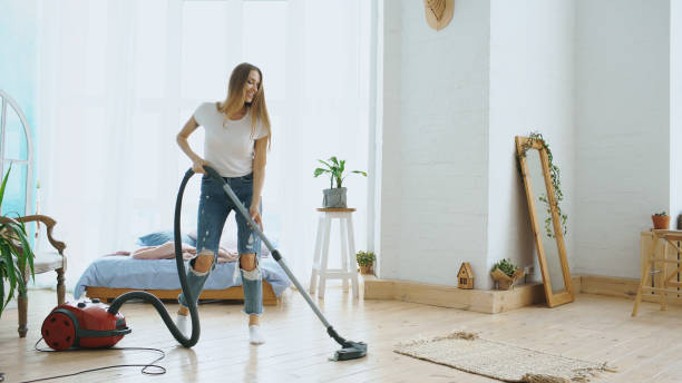 Young woman having fun cleaning house with vacuum cleaner dancing and singing